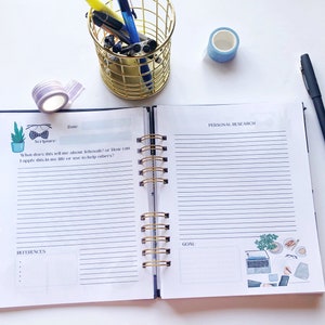 May include: Open spiral-bound journal with lined pages, gold spiral, and decorative stickers. The journal is open to a page with the text "Scripture" and "Personal Research." A gold wire pen holder and washi tape are also visible.