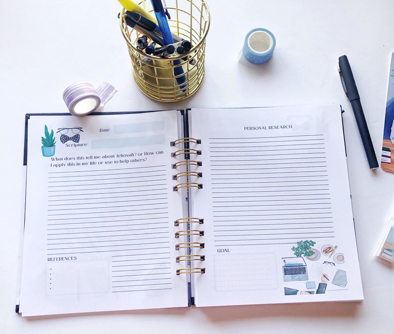 May include: Open spiral-bound journal with lined pages, gold spiral, and decorative stickers. The journal is open to a page with the text "Scripture" and "Personal Research." A gold wire pen holder and washi tape are also visible.