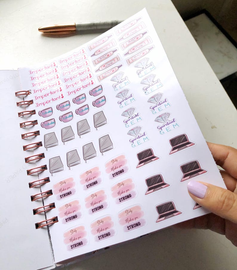 May include: A planner with sticker sheets featuring various designs. Stickers include the words "Important!", teacups, books, laptops, and the phrase "Study Makes You Strong". A rose gold pen rests on the planner.