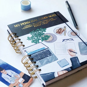 May include: A spiral-bound notebook with the text "MY PERSONAL STUDY NOTE" in gold lettering. The cover features illustrations of a laptop, food, and a person writing. A blue washi tape roll and a black pen are also visible.