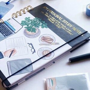 May include: A spiral-bound notebook with the text "MY PERSONAL STUDY NOTES" in gold lettering. The cover features illustrations of a laptop, potted plant, coffee, and cake. A black elastic band secures the notebook.