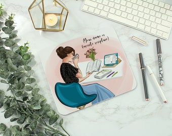 May include: A pink and white desk pad with a cartoon illustration of a woman sitting at a desk with a cup of coffee, a book, a laptop, and a bouquet of flowers. The text "(Your name or favorite scripture)" is at the top of the pad.