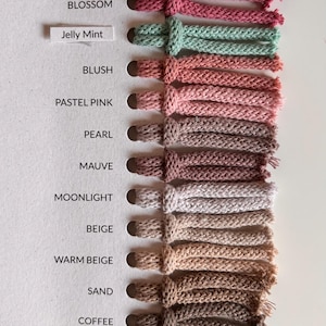 May include: A color swatch card featuring thirteen knotted yarn samples in various shades including wine red, burgundy, blossom, jelly mint, blush, pastel pink, pearl, mauve, moonlight, beige, warm beige, sand, coffee, and dusty rose with labels.