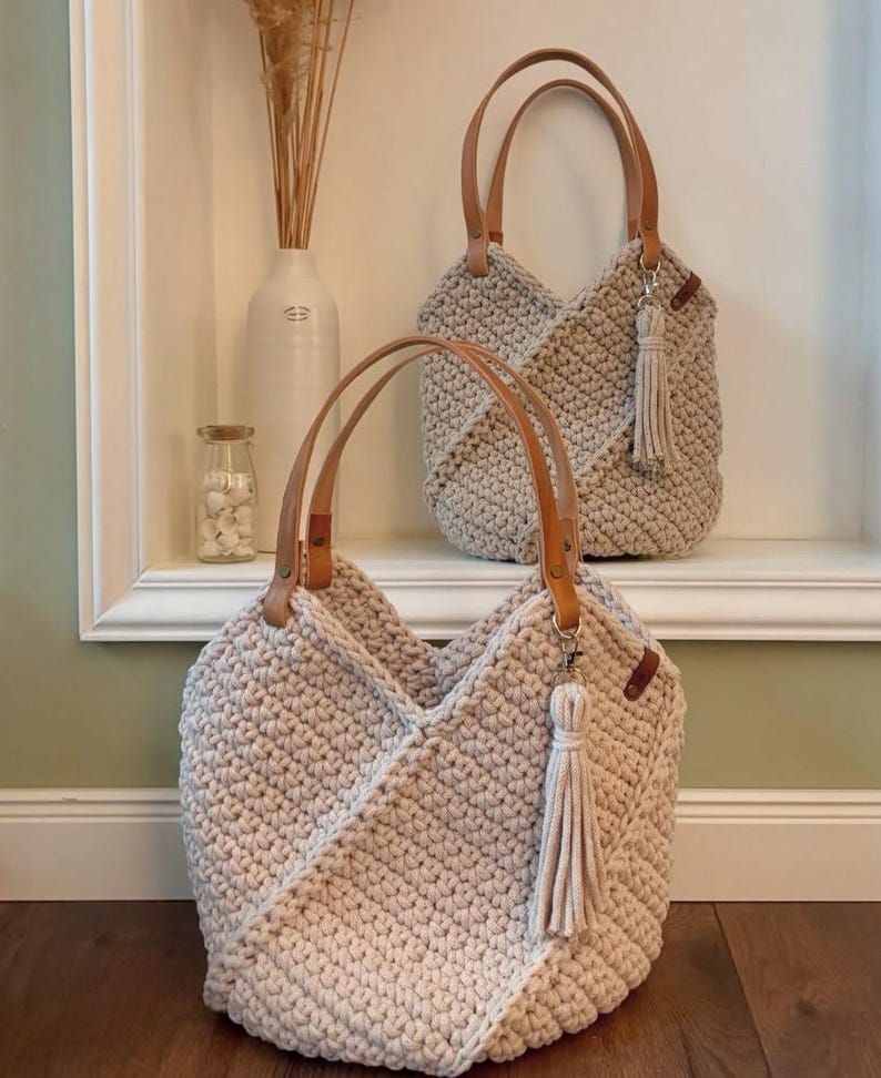 K&ouml;nnte beinhalten: Zwei beige geh&auml;kelte Tragetaschen mit strukturiertem Stichmuster, hellbraunen Ledergriffen und einer passenden beigen Quaste an einem silbernen Metallverschluss. Die Taschen haben ein V-f&ouml;rmiges Frontdesign und bestehen aus dickem Kordelmaterial.