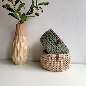 Puede incluir: Dos cestas de crochet, una verde y otra beige, con etiquetas de cuero que dicen "Made with Love". Las cestas est&aacute;n apiladas una encima de la otra sobre una superficie blanca.