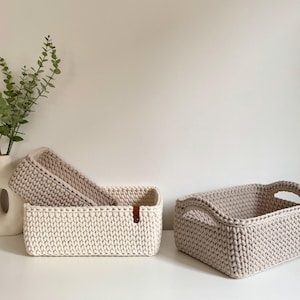 Könnte beinhalten: Ein Set aus drei Keramikbechern mit gesprenkelter, matter Oberfläche. Die Becher sind in Creme-, Hellbraun- und Dunkelbrauntönen gehalten. Jeder Becher hat ein schlichtes Design und einen abgerundeten Henkel.