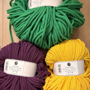 May include: Three skeins of braided cord in jade green, aubergine, and canary yellow. Each skein features a white paper label with the color name, a barcode, and technical specifications including 8-10mm thickness and 100m length.