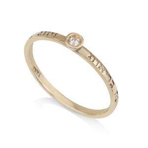 Puede incluir: Un anillo de oro con un pequeño diamante engastado en el centro. El anillo está inscrito con texto hebreo.