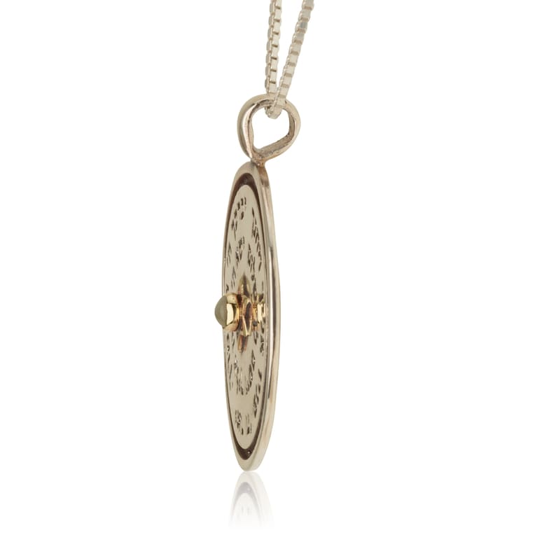 Puede incluir: Collar con colgante de plata en forma de disco redondo adornado con una estrella de David y texto hebreo. El disco tiene un acento dorado en el centro.