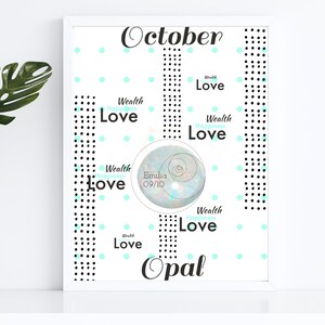 Può includere: Una stampa incorniciata bianca con la parola "Ottobre" in corsivo nero. La stampa presenta una pietra preziosa di opale blu chiaro con il nome "Emilia" e la data "09/10" scritta su di essa. La stampa è circondata da uno schema di punti neri e punti blu chiaro. Le parole "Ricchezza, Felicità, Amore" sono ripetute attorno alla pietra preziosa di opale blu chiaro in un carattere blu chiaro.