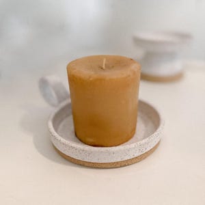 May include: A white ceramic candle holder with a speckled finish and a beige candle inside.