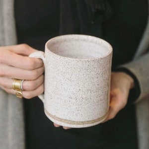 May include: A white ceramic mug with a speckled glaze and a brown rim. The mug is large and has a handle.