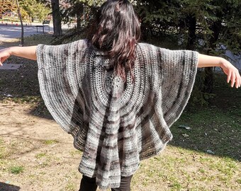 Peut inclure: Un châle en crochet gris et brun avec un motif circulaire. Le châle est drapé sur les épaules d'une personne debout à l'extérieur.