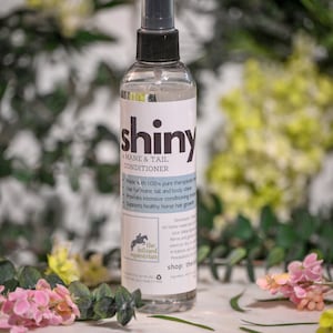 May include: A clear bottle of "shiny" mane and tail conditioner with a black label and a white horse logo. The label reads "the infused equestrian" and "shop: theinfusedequestrian.com".