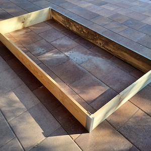 May include: A wooden raised garden bed with metal corner brackets. The bed is empty and sits on a patio.