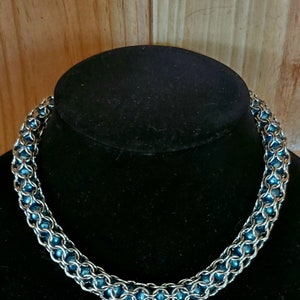 May include: A silver chain necklace with blue beads. The necklace is on a black velvet display stand.