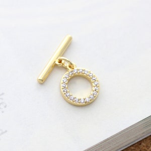 Può includere: Chiusura a scorrimento dorata con un ciondolo circolare tempestato di strass trasparenti.