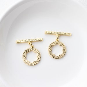 Peut inclure: Deux fermoirs à glissière en métal doré avec un pendentif rond décoratif. Chaque cercle a un motif de fleur découpée et une surface texturée.