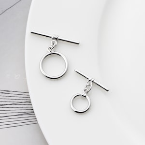 Può includere: Due chiusure a scatto argentate con anelli rotondi. Le chiusure sono in metallo e hanno una finitura lucida.