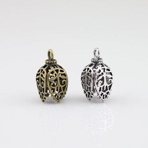 May include: Two ornate metal pendant caps, one in antique gold and one in silver, with a filigree design. The caps are shaped like a bell with a loop at the top for hanging.