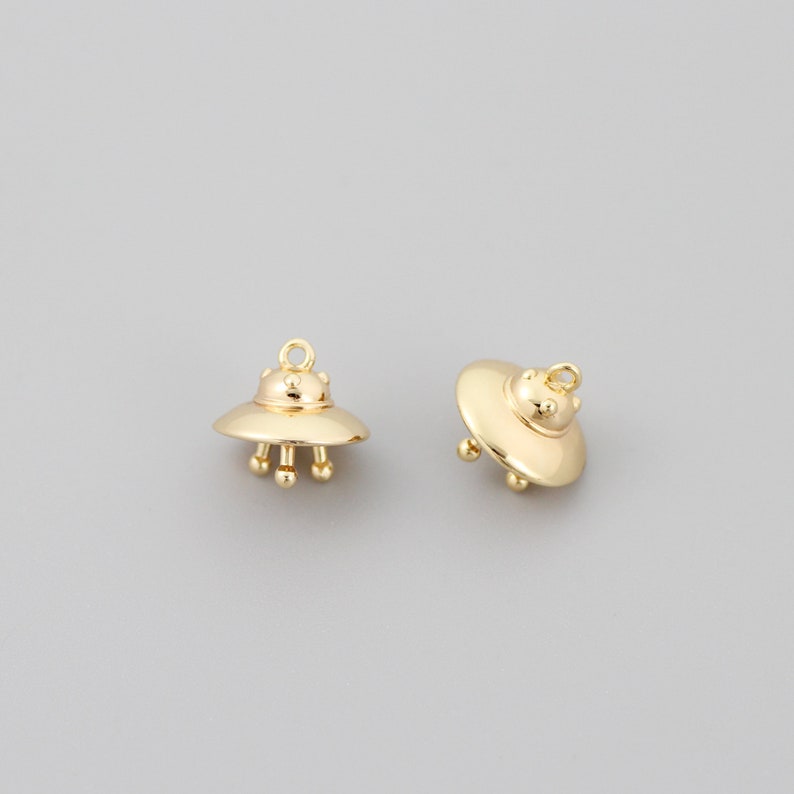 Op de afbeelding: Twee gouden UFO-bedels met een lus om aan een ketting of armband te bevestigen.