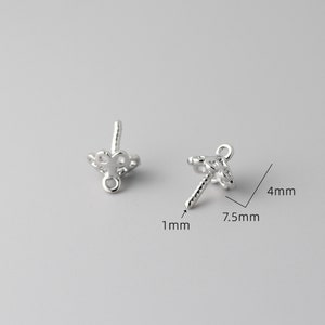 May include: Two silver-toned earring findings with a decorative design. The findings are 7.5 mm wide and 4 mm tall. The findings have a 1 mm diameter post.