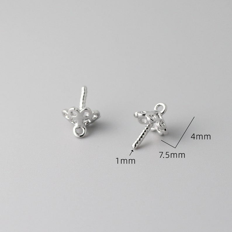 May include: Two silver-toned earring findings with a decorative design. The findings are 7.5 mm wide and 4 mm tall. The findings have a 1 mm diameter post.
