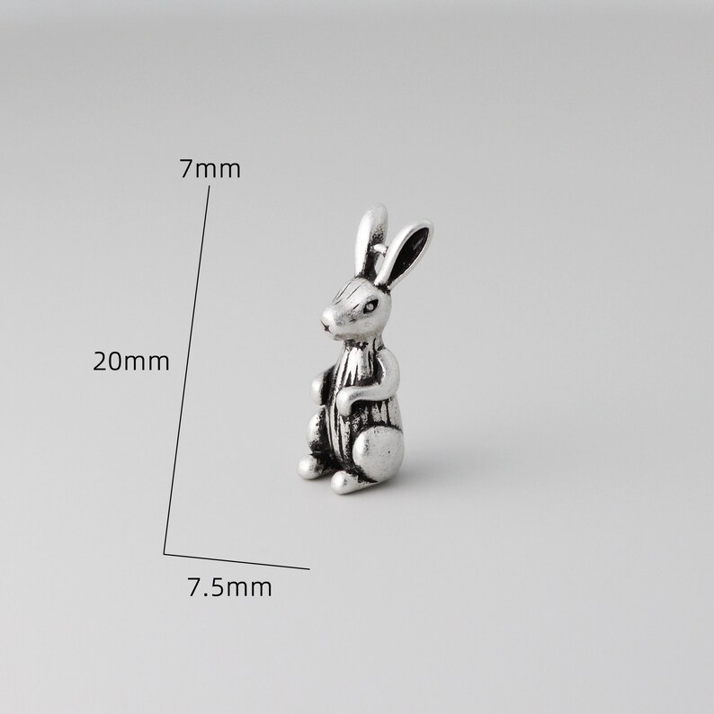 Peut inclure: Petite figurine argent&eacute;e repr&eacute;sentant un lapin, mesurant 20 mm de haut, 7,5 mm de large et 7 mm d'&eacute;paisseur. Le lapin est repr&eacute;sent&eacute; assis, les oreilles dress&eacute;es. La figurine pr&eacute;sente des d&eacute;tails et un aspect l&eacute;g&egrave;rement vieilli.
