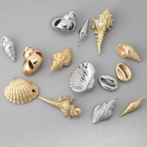 May include: A collection of various seashell charms in gold and silver tones. The assortment includes conch shells, scallop shells, and other sea-inspired designs. These decorative charms are ideal for jewelry making or craft projects.