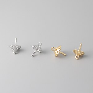 May include: Three silver and gold bead caps with a decorative design. The bead caps have a loop at the top and a pin at the bottom.