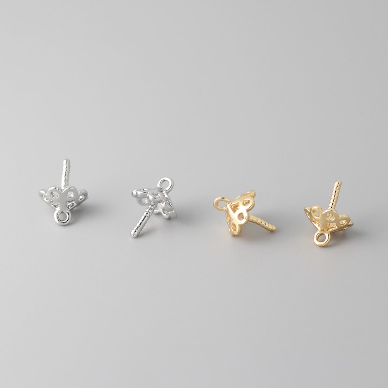 May include: Three silver and gold bead caps with a decorative design. The bead caps have a loop at the top and a pin at the bottom.