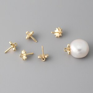 May include: Five gold-toned earring findings with a decorative starburst design and a white pearl pendant.
