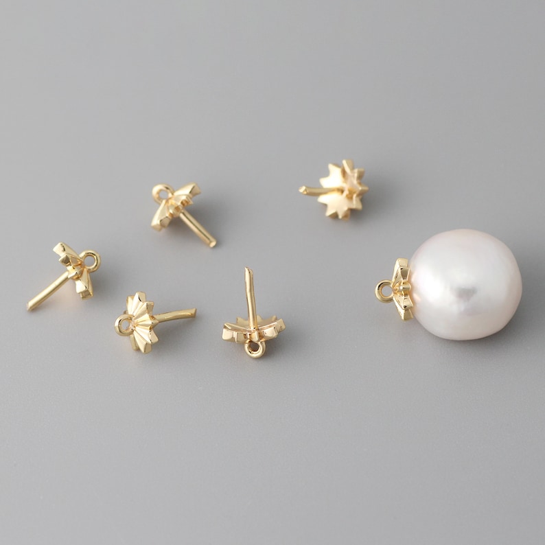 May include: Five gold-toned earring findings with a decorative starburst design and a white pearl pendant.