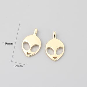 Op de afbeelding: Twee goudkleurige alien-hoofdcharms, elk 19 mm hoog en 12 mm breed. De charms zijn uitgesneden in de vorm van een alien-hoofd met grote ogen en een kleine mond.
