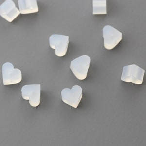 May include: A collection of small, white, heart-shaped silicone molds. The molds are scattered on a gray surface.
