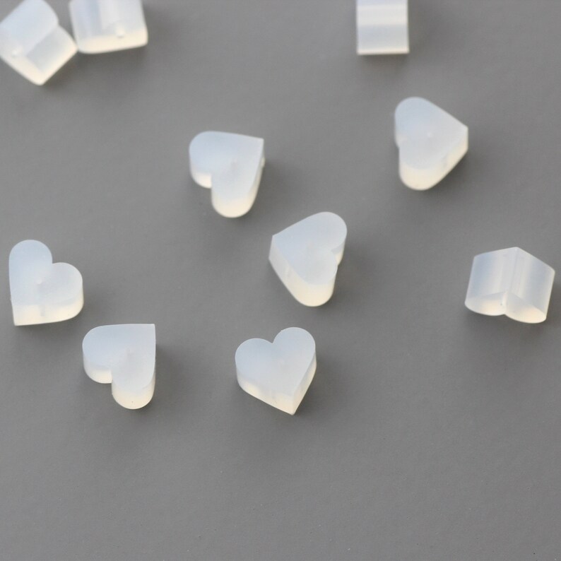 May include: A collection of small, white, heart-shaped silicone molds. The molds are scattered on a gray surface.