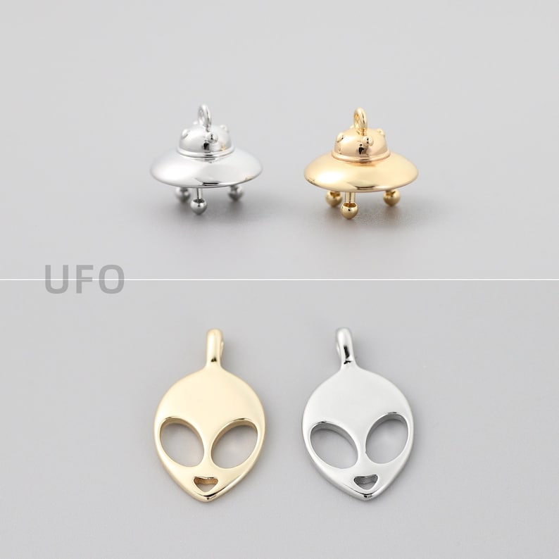 Op de afbeelding: Twee UFO-bedels, een in zilver en een in goud. De UFO's hebben de klassieke vorm van een vliegende schotel met een gewelfde bovenkant en een ring om op te hangen. De bedels zijn perfect om sieraden of knutselwerk met een vleugje fantasie te versieren.