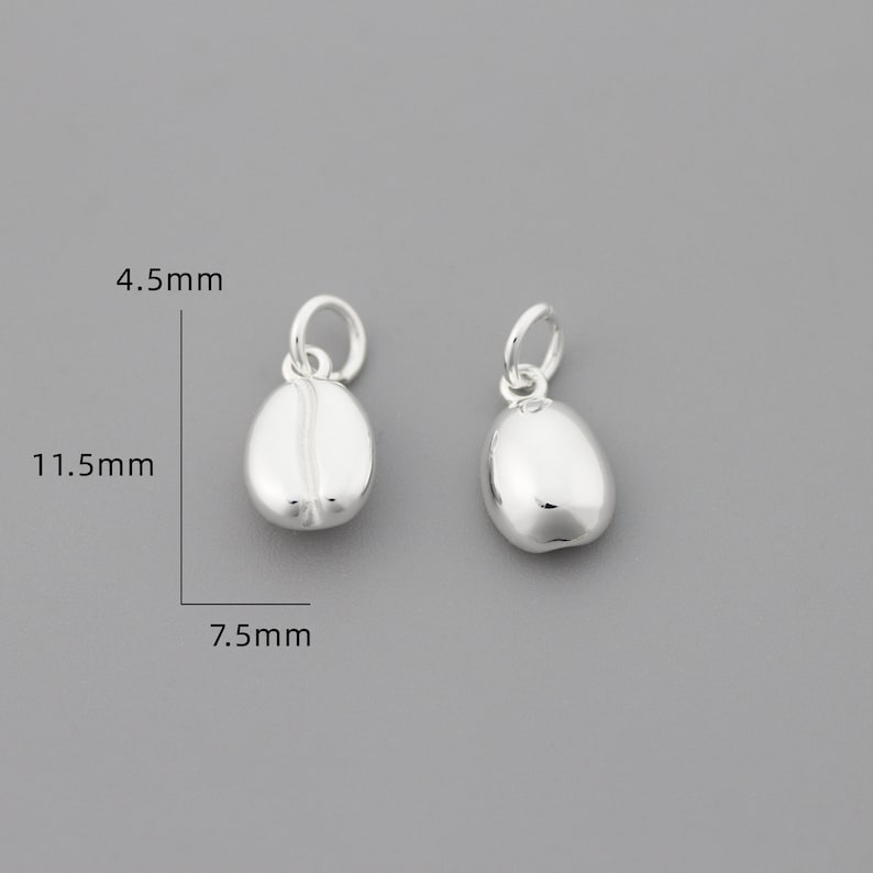 K&ouml;nnte beinhalten: Zwei silberne Kaffebohnen-Anh&auml;nger, jeder 11,5 mm lang, 7,5 mm breit und 4,5 mm hoch.