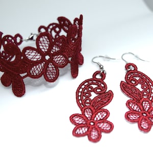 May include: A set of red lace jewelry featuring a choker necklace and a pair of dangling earrings. The lace is delicate and intricate, with a floral design.