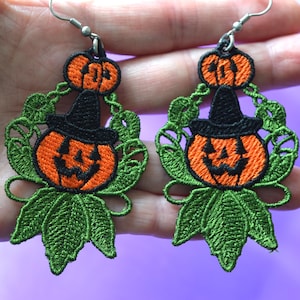 Może przedstawiać: Haftowane kolczyki na Halloween z pomarańczowymi dyniami w czarnych kapeluszach czarownic. Kolczyki mają zielone liście i winorośl oraz srebrne haczyki na uszy. Zabawny i świąteczny dodatek na sezon jesienny.