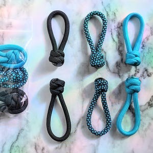 Peut inclure: Divers tirettes de fermeture éclair en corde tressée, disponibles en noir, bleu sarcelle et bleu. Les tirettes ont une conception en boucle et sont présentées individuellement et dans un sac en plastique transparent. Fond marbré. Mesures en centimètres.