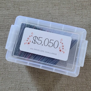 May include: A clear plastic container filled with envelopes. The container has a label that says "$5,050 100 ENVELOPE CHALLENGE".