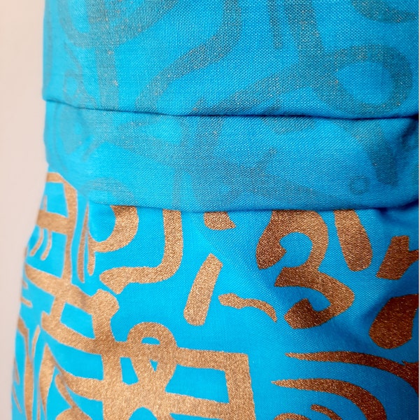 Tissu pour habillement turquoise imprimé avec de la calligraphie dorée. Convient à l'habillement pour la couture de jupes drapées. Par 50 cm