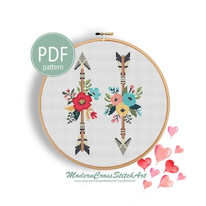 Puede incluir: Un patrón de punto de cruz con dos flechas coloridas con detalles florales. El patrón está en un aro de bordado de madera y está listo para ser cosido.