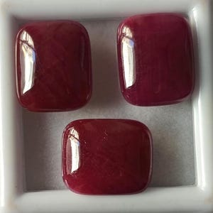 May include: Three red gemstone cabochons in a square shape, displayed in a white box.