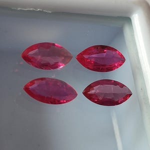 May include: Four marquise-shaped gemstones, each a vibrant pink, are displayed on a white surface. The gemstones are arranged in two rows of two.