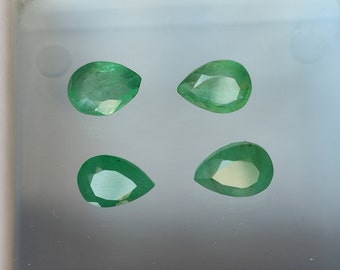 Puede incluir: Cuatro piedras preciosas de esmeralda en forma de pera, cada una con un tono verde y un corte facetado, se muestran sobre una superficie blanca.