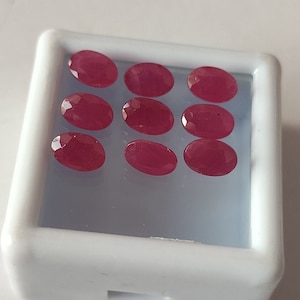 May include: Ten oval-shaped, red gemstones in a white display case.