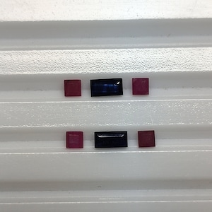 May include: Six loose gemstones arranged in two rows on a white surface. The top row has two red gemstones and one blue gemstone. The bottom row has two red gemstones and one blue gemstone.