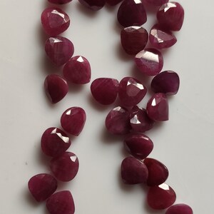 May include: A collection of 25 faceted ruby gemstone beads in a teardrop shape. The beads are a deep red color and have a polished finish.